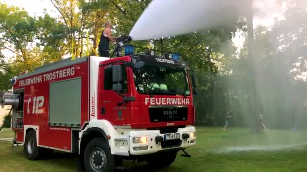 Deutsches Feuerwehrauto Versprüht Wasser Für Kinder Und Bäume Einem Heißen — Stockvideo