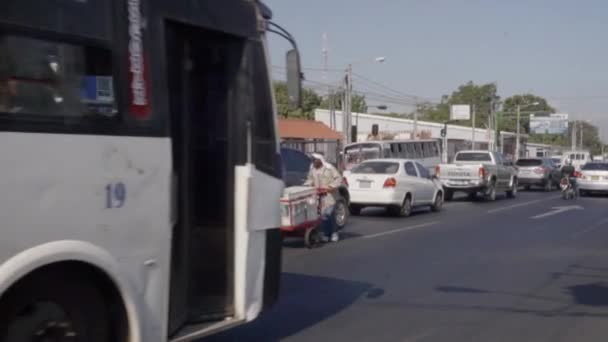 地元の男が通りに沿ってカートを押している間に白いバスが走っている — ストック動画