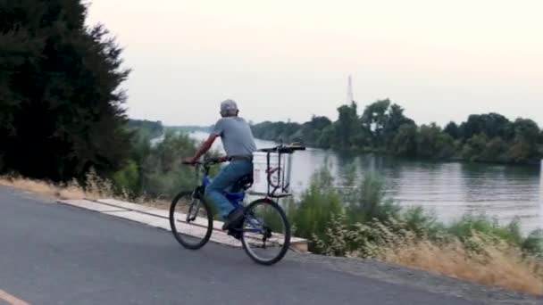 Άνθρωπος Ποδηλασία Κατά Μήκος Του Ποταμού Κατά Διάρκεια Του Ηλιοβασιλέματος — Αρχείο Βίντεο