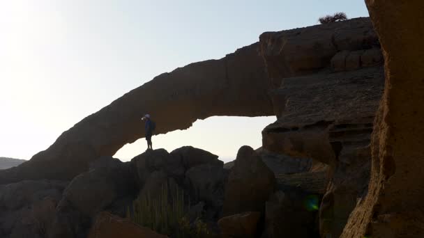 背包客男子站在Tenerife 的一个天然石拱边的岩石上喝水 Hd在版本中的剪切和缩放 — 图库视频影像