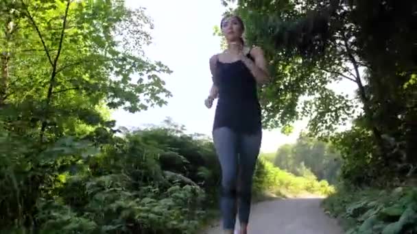 一个女人在公园的小径上慢跑 一个身材瘦小的女孩 一头长长的金发 穿着灰色紧身衣 头戴黑色上衣 — 图库视频影像