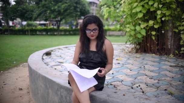 Egy dögös ázsiai lány tanul egy fa alatt az egyetemi egyetem területén, könyvet olvas.
