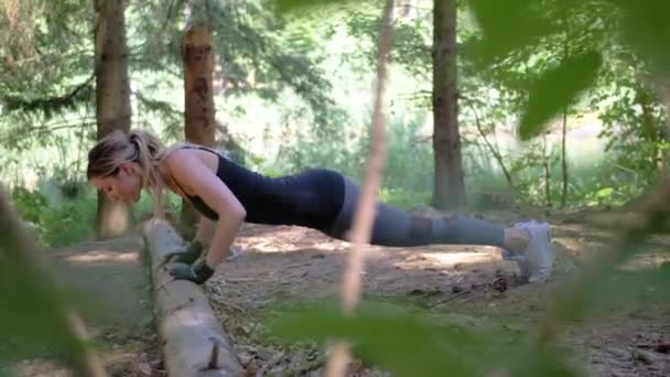 一个女人穿着手套和运动服在公园里俯卧撑 明亮的阳光和绿树为她的锻炼提供了一个良好的环境 完全正确的 慢动作 — 图库视频影像