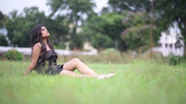 A beautiful and hot Asian girl wearing short Black dress is relaxing on grass with light  breeze of wind and combing her hair with fingers