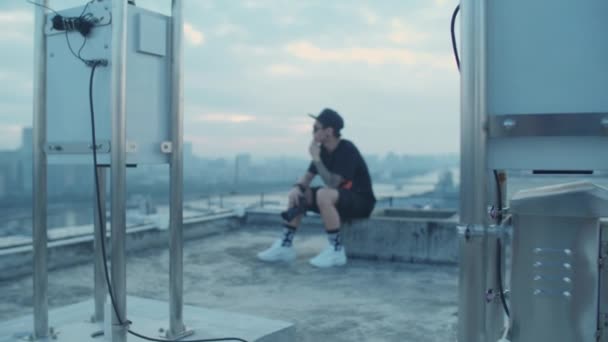 早朝に屋上に座っている間に都市部のダウンタウンをキャプチャ若いアジアの写真家のオープンショット — ストック動画
