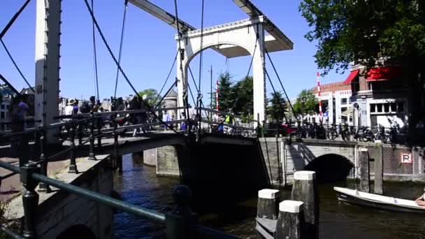 人々はオランダのアムステルダムの運河橋を渡って歩く ボートはオランダのアムステルダムの歩行橋の下に行く — ストック動画
