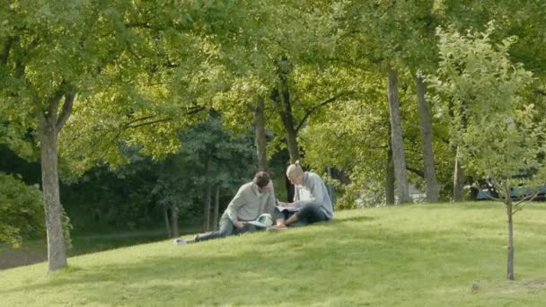 Jeune Couple Étudiant Sur Monticule Herbeux Avec Des Arbres Proximité — Video