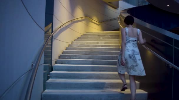 一个穿着花蝴蝶裙的年轻貌美的女人从容地走上楼梯 然后加快步伐 背景是一座现代建筑 — 图库视频影像