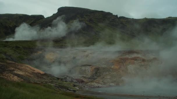 アイスランドの風景 地熱温泉の蒸気煙が上がり 遠くから撮影した写真家の姿 広角レンズのショット 左から右へのカメラパン — ストック動画