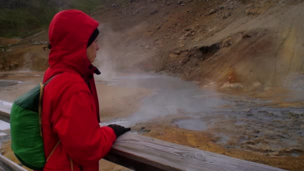 劇的なアイスランドの風景 地中から湧く地熱温泉の蒸気煙 現場を見ている赤いジャケットを着た女性旅行者 クリスヴィク セルトゥン地域 中程度のショット — ストック動画