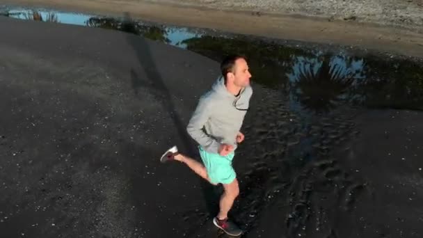 ニュージーランドのオークランドでビーチを走っている若い男の空中追跡ショット — ストック動画