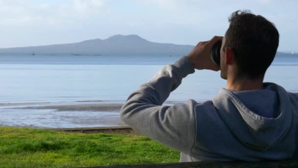 Joven Hombre Caucásico Tomando Café Sentado Banco Playa Mirando Isla — Vídeo de stock