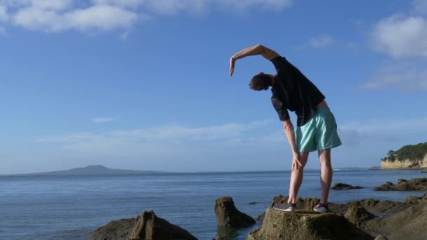 Młody Sprawny Mężczyzna Rozciągający Się Skalistej Plaży Auckland Nowa Zelandia — Wideo stockowe