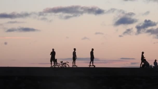ハワイのホノルルの人々の間で日没に出発する2人のスケートボーダー — ストック動画