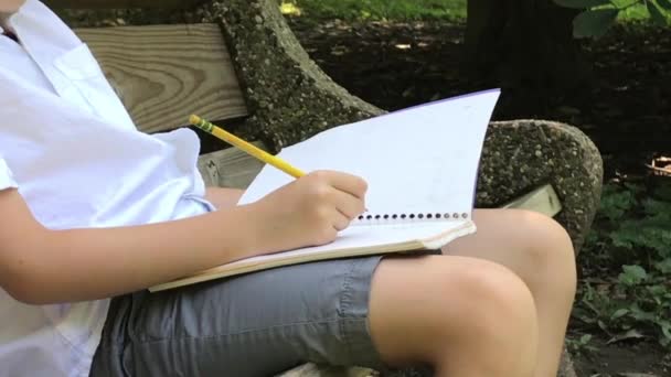 Çocuk Bir Bankta Oturuyor Bir Deftere Yazıyor — Stok video
