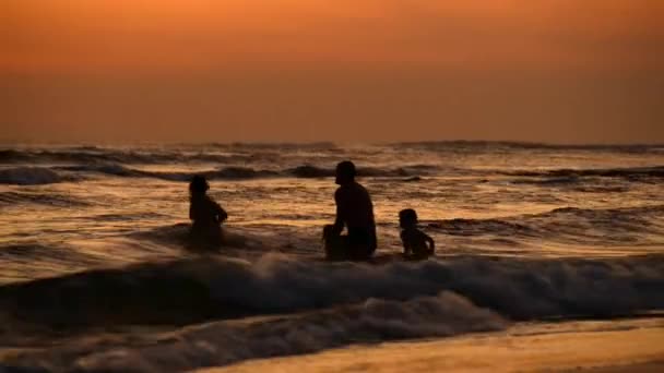 Rodina s malým dítětem hraje v západu slunce oceánu s velkými vlnami