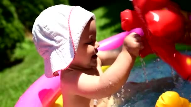 Toddler gets amused and excited by playing with toys and splashing water in a small pool set in a garden