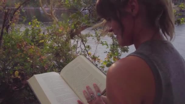 かわいいですヒップスター女の子読書地元の公園で本によって川 — ストック動画