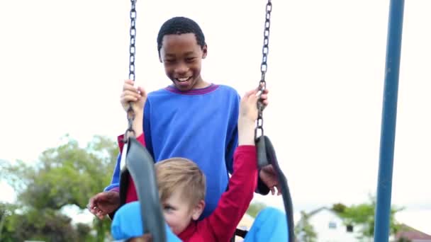 Interracial friendship - boys laugh and play on the swings at the park