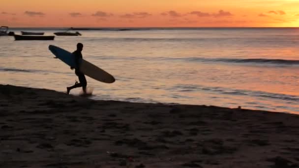 4K Surfař běží na pláži se surfařem do moře během tropického západu slunce
