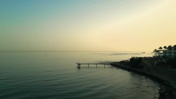 空中ショットがダウンして移動します 夕暮れ時に海岸線から伸びる静かな桟橋の風景 — ストック動画