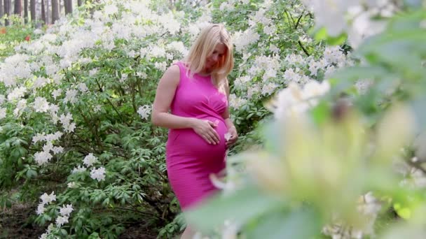 Těhotná žena v šatech drží ruce na břiše na přirozeném pozadí rododendron v letní den. Pojem těhotenství, mateřství.