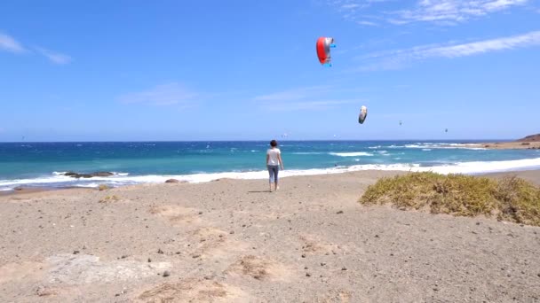 Denize Doğru Yürüyen Bir Kadın Rüzgar Sörfçülerine Uçurtma Sörfçülerine Bakıyor — Stok video