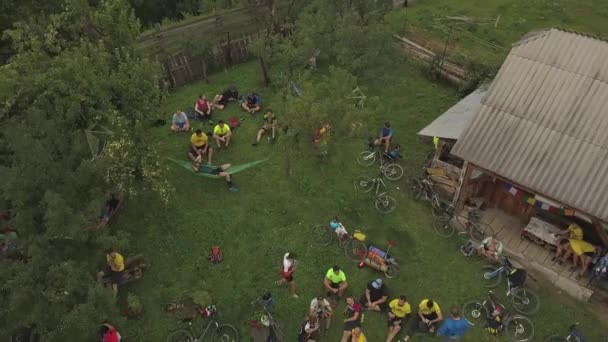 ルーマニアの田舎でマウンテンバイクレースをした後 木製の建物の近くの丘の上に座っている多くの人々の空中パン — ストック動画