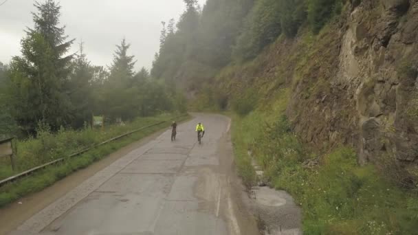 ルーマニアの田舎でのサイクリングレース中に霧深い山道を自転車で駆け上がる2人の自転車の前でドローンが撃たれました — ストック動画