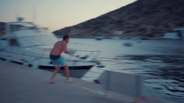 ギリシャのビーチの近くのドックで水の中に潜る若い観光客 ギリシャの人々の幸せな顔は彼らの友人と楽しむ — ストック動画