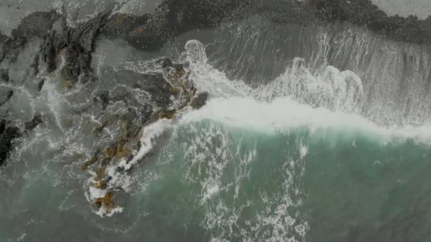 波が岩の上を衝突して岩の上をまっすぐ飛んでいるのを見る遅いドローンショット — ストック動画