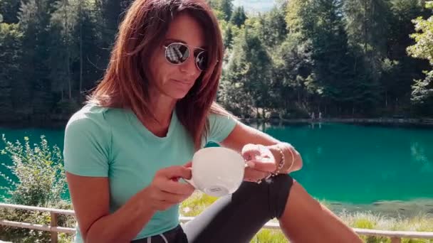 Sportovní a atraktivní starší žena s kávou, mluvení a relaxaci u jezera v přírodě po cvičení v létě
