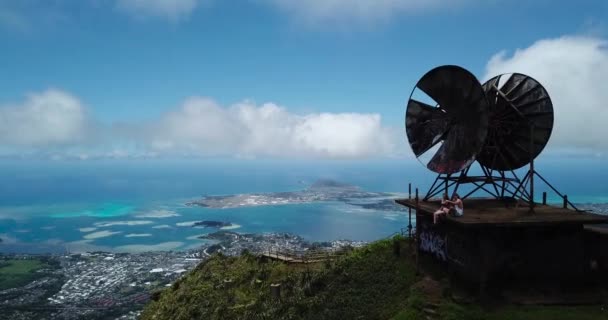 オアフ島の空気中のドローン4000Ft天国への階段の山道のショットを取得し ショットは古い衛星と建物の上に座っているカップルを示しています — ストック動画