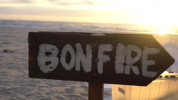 ビーチでのたき火の標識の背景に日没とキャンプファイヤーを指している — ストック動画