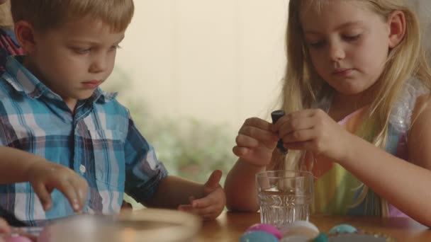 水のガラスに染料ボトルを絞る若い女の子のスローモーションショット — ストック動画