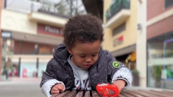 Afroeuropean Baby Playing Red Plastic Toy Car Wood Bench Wearing — Stockvideo