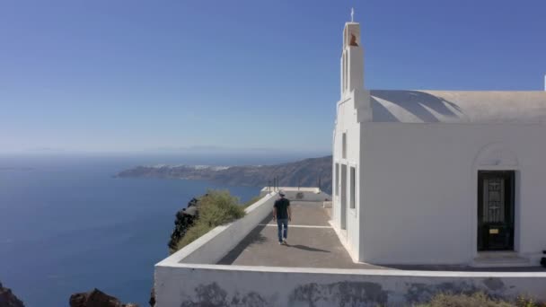 Aéreo Homem Caminha Lado Uma Igreja Santorini Grécia Dia Ensolarado — Vídeo de Stock