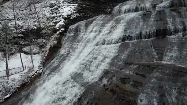 雪の冬の季節にロッキークリフに流れる冷たい水の空中ビュー バターミルクフォールズ州立公園 ニューヨーク州 ドローンショット — ストック動画