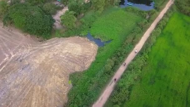 カンボジアのシェムリアップの農村部の未舗装の道路に沿ってスクーターに乗る観光客 空中傾斜アップショット — ストック動画