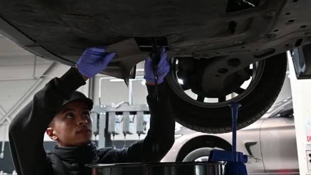 Молодой Механик Откручивает Осушает Старое Масло Поднятого Автомобиля Медленное Движение — стоковое видео