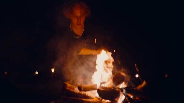 男は夜 たき火でキャンプファイヤーに座って 火災を見て 暗い真夜中のキャンプファイヤーたき火 — ストック動画
