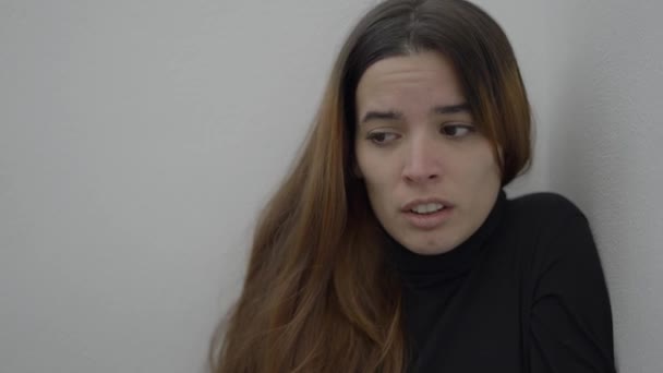 恐怖の表情で壁に座っている若い女性のクローズアップ — ストック動画