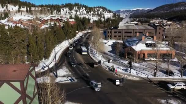 雪に覆われたアメリカのコロラド州の町の道路上で空中撮影昼前に前景に赤レンガ造りの建物でバックグラウンドで山をカバー — ストック動画