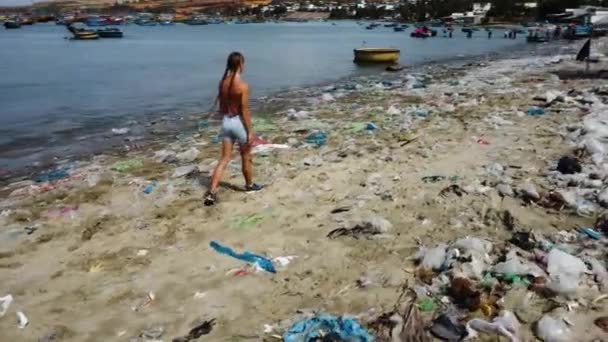 Young woman walking on a lonely tropical sandy beach covered in plastic garbage waste trash, ocean pollution, climate change in Asia