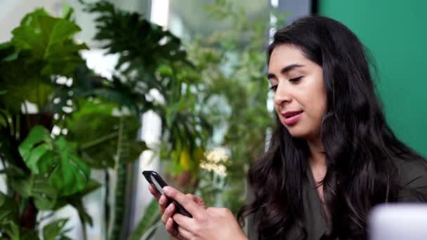 ラテンアメリカの若いフリーランス女性のビデオ通話は 5Gインターネットデータに接続された彼の現代的なスマートフォンデバイスとのオンライン会議でチャット コワーキングスペースからのリモートワーク — ストック動画