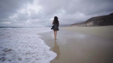 Multiracial mixed race young latin woman walking alone on ocean sand beach in Fuerteventura canary island Spain, creative photographer exploring new touristic spot