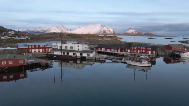 ノルウェー ロフトテンの雪の山の背景を持つ港や町の周りの空中ビュー ドローンショット — ストック動画