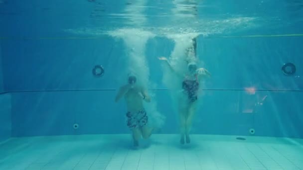 水中のカップルは 現代の水着とダイビングマスクガラスでスイミングプールの水に飛び込み 無呼吸で遊ぶ準備ができて — ストック動画
