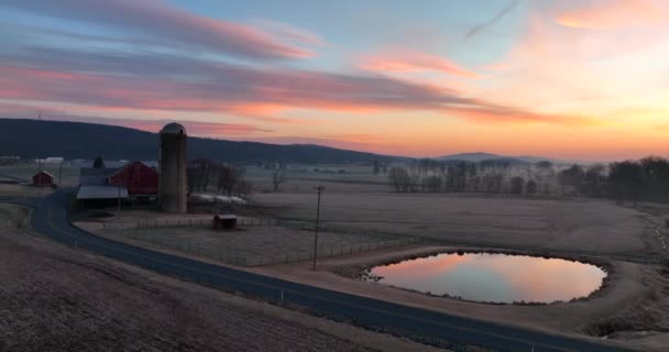 Zimní scéna hnědé louky na farmě. Vzestup vzduchu stodoly a sila. Východ slunce se odráží v jezírku. USA zemědělství téma.