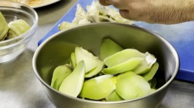 Enginar yaprakları kaseye düşerken, aşçı onları restoranda kurutuyor.